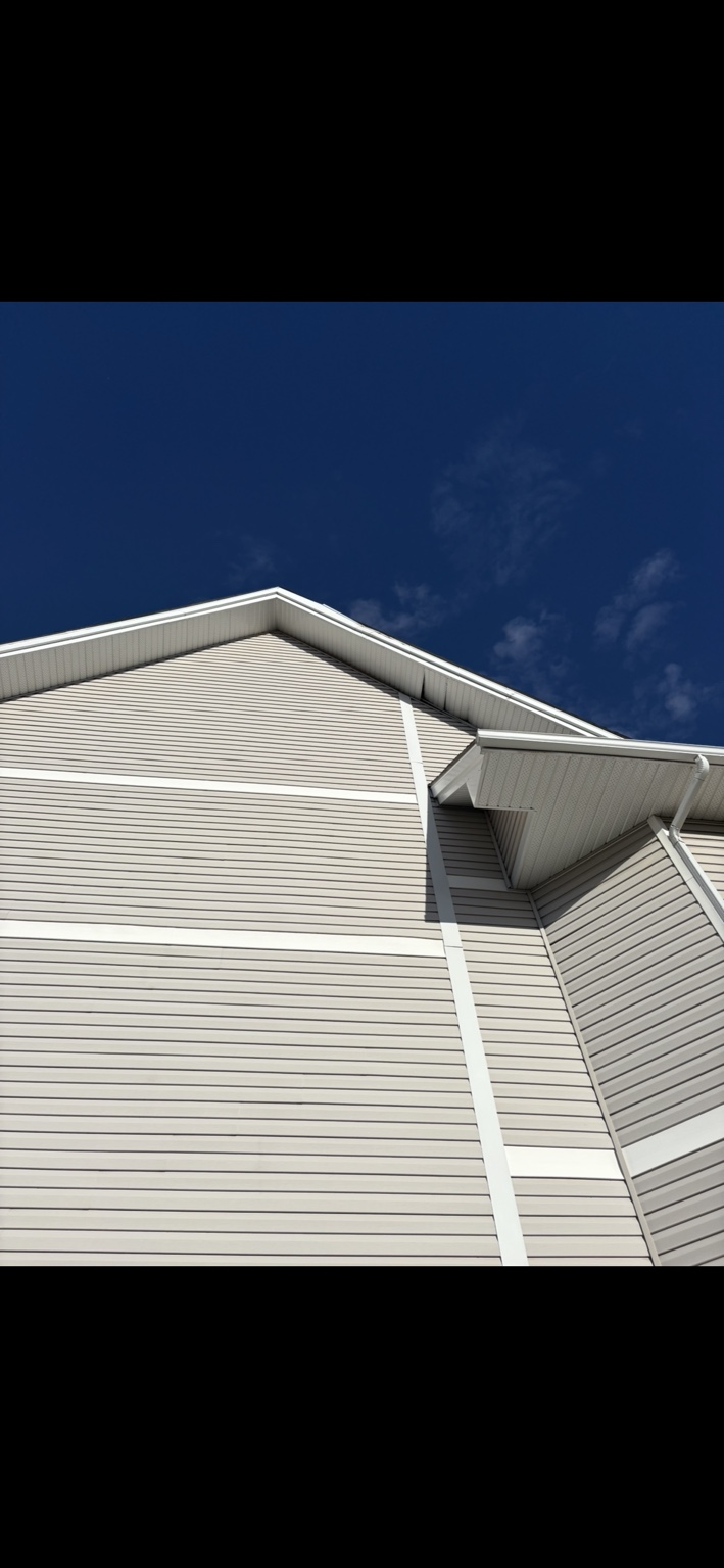 Wind-damaged soffit panels coming loose beneath the upper roof edge